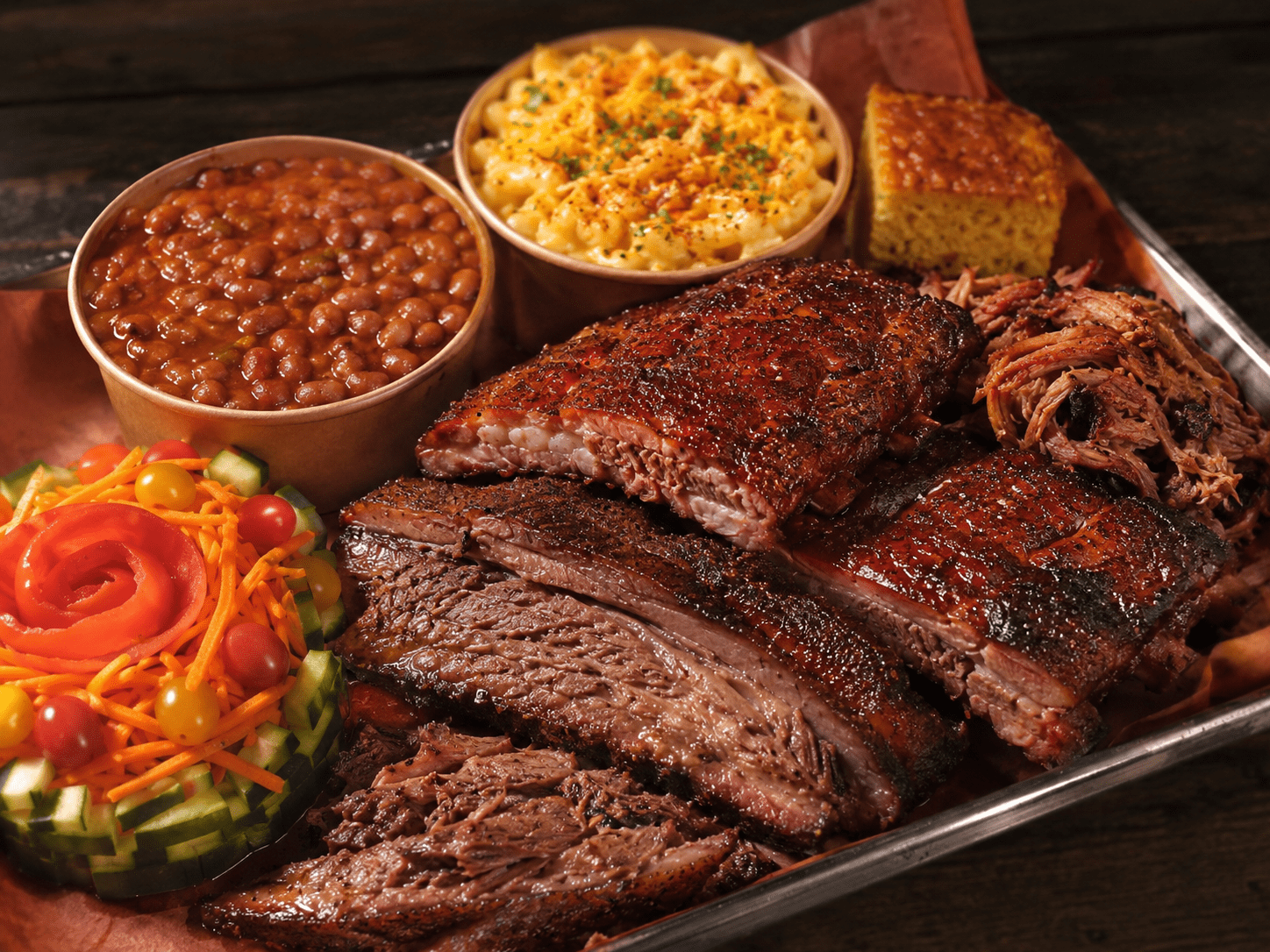 BBQ dinner combo platter with brisket, ribs, pulled pork, baked beans, mac and cheese, cornbread, and fresh salad